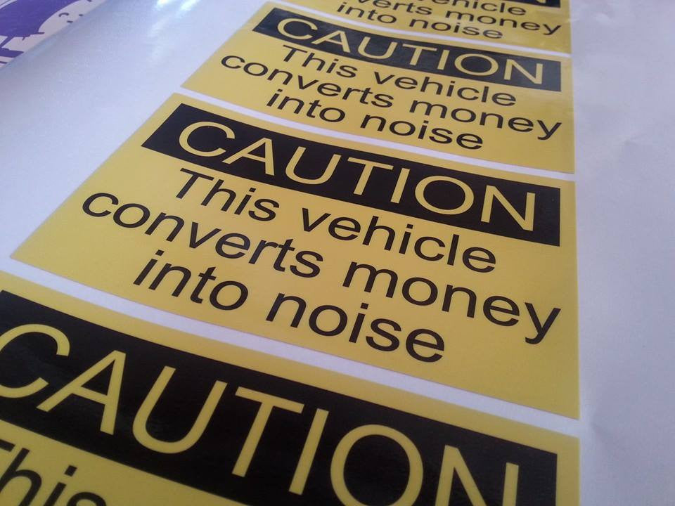 "CAUTION This vehicle converts money into noise" sticker.
